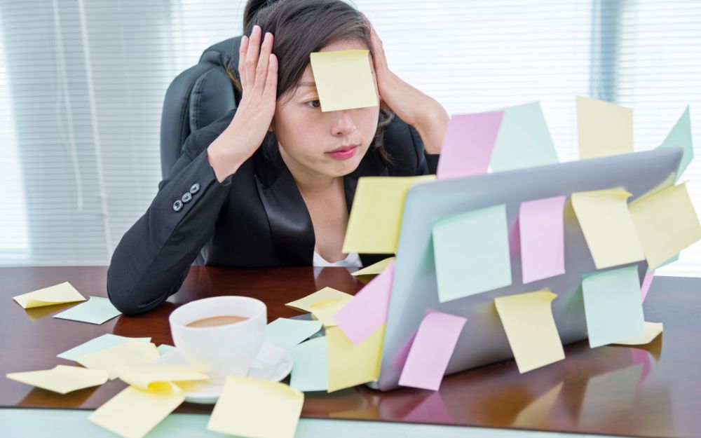 Une femme stressée devant son ordinateur avec des post-it collés sur le visage